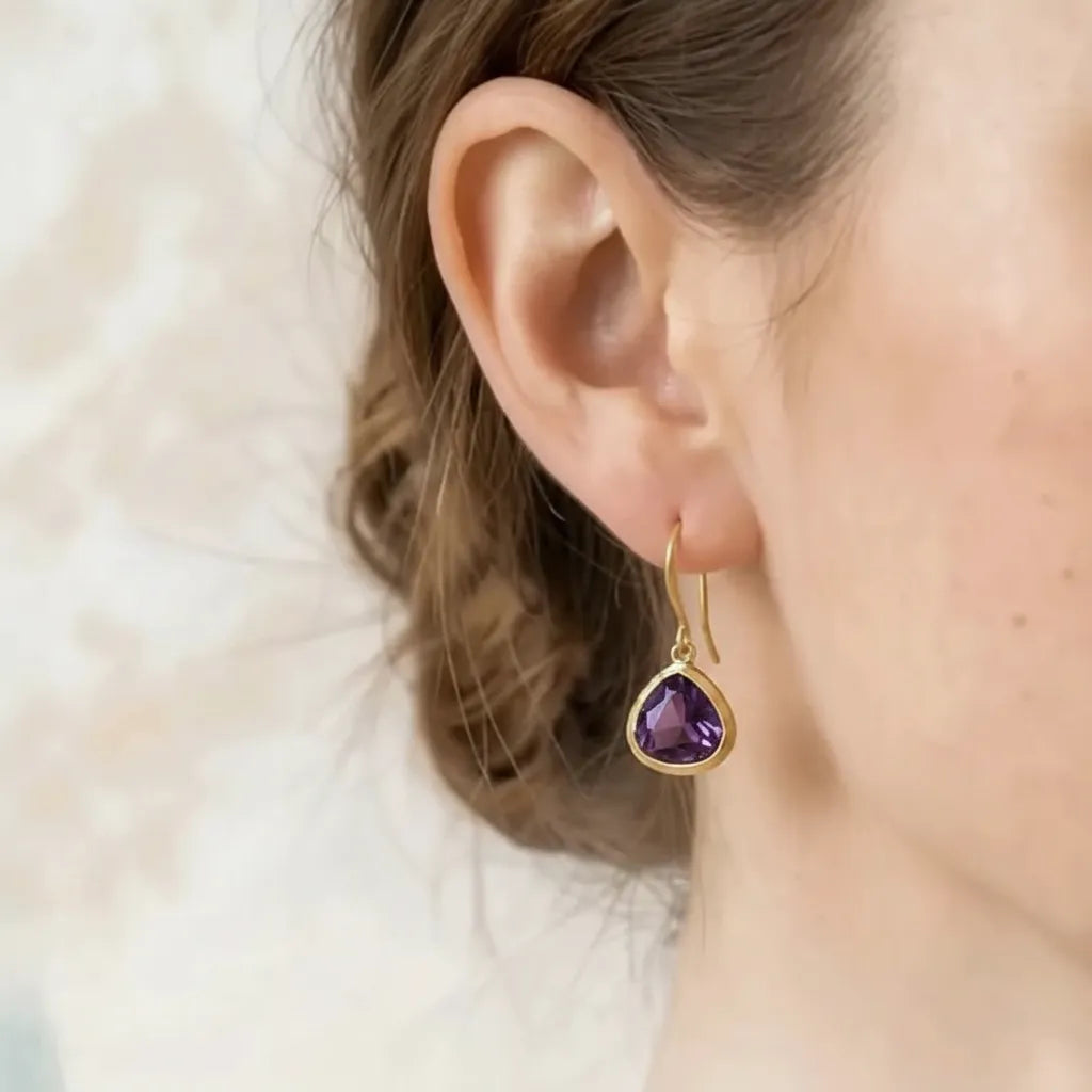 Woman wearing amethyst mini drop earrings in gold, February birthstone jewelry