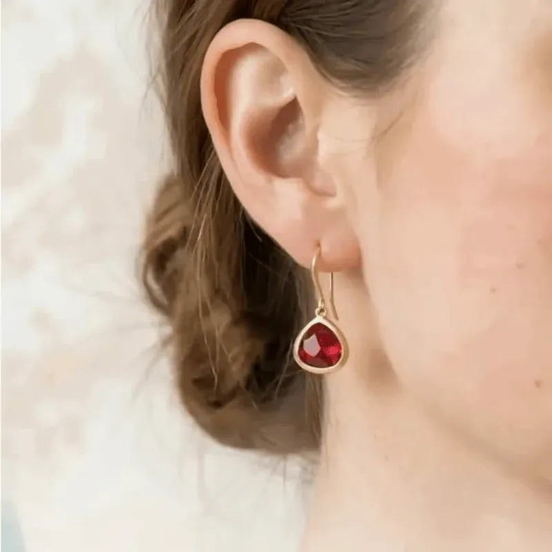 Gold earrings with red gemstones worn by a person with blurred background