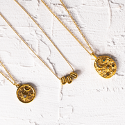 Three gold necklaces with circular pendants on a white textured surface