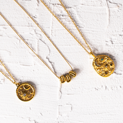 Three gold necklaces with circular pendants on a white textured surface