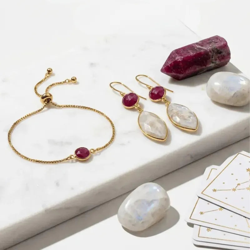 Gold jewelry set with red gemstones on a marble surface