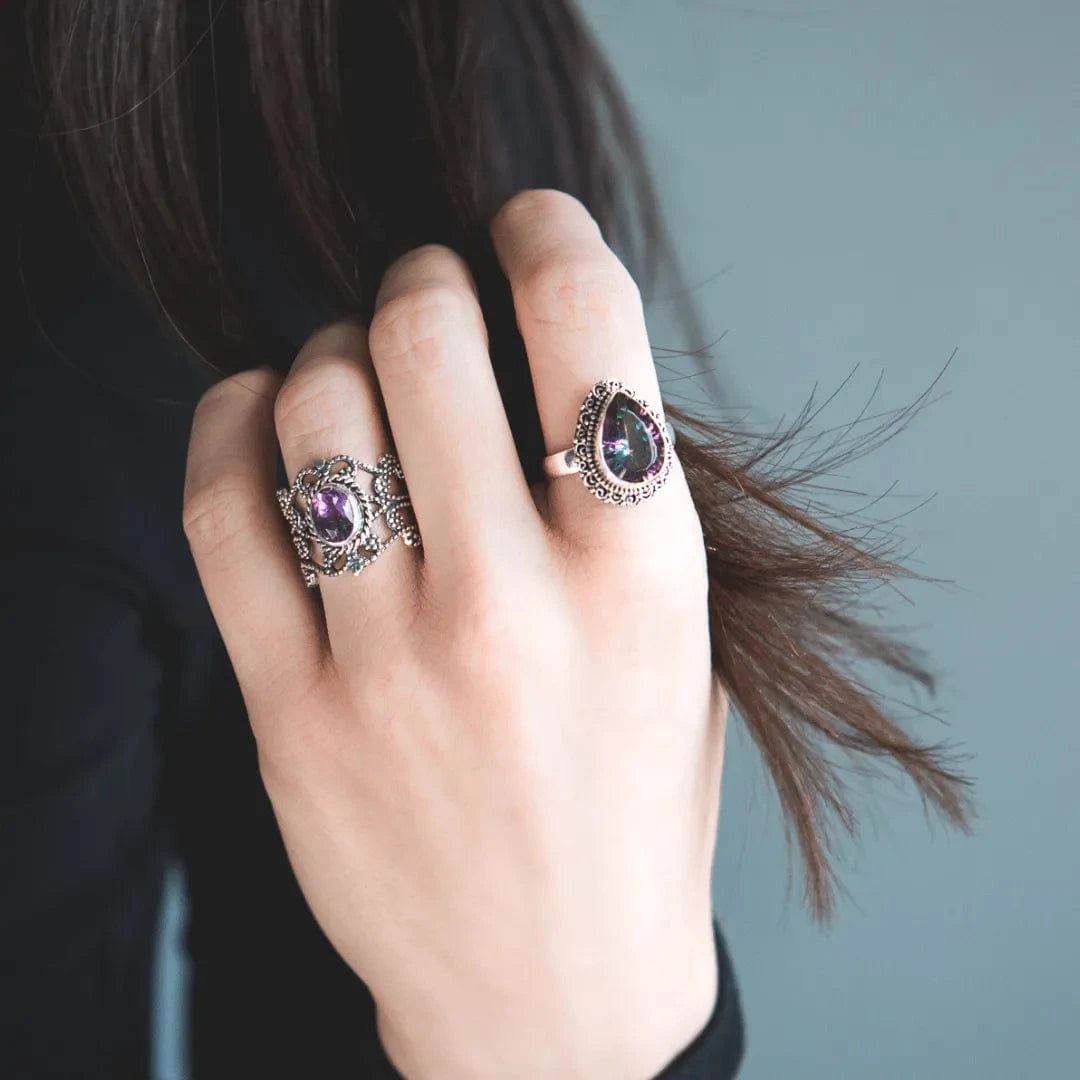 Hand wearing two ornate rings with purple gemstones against a neutral background