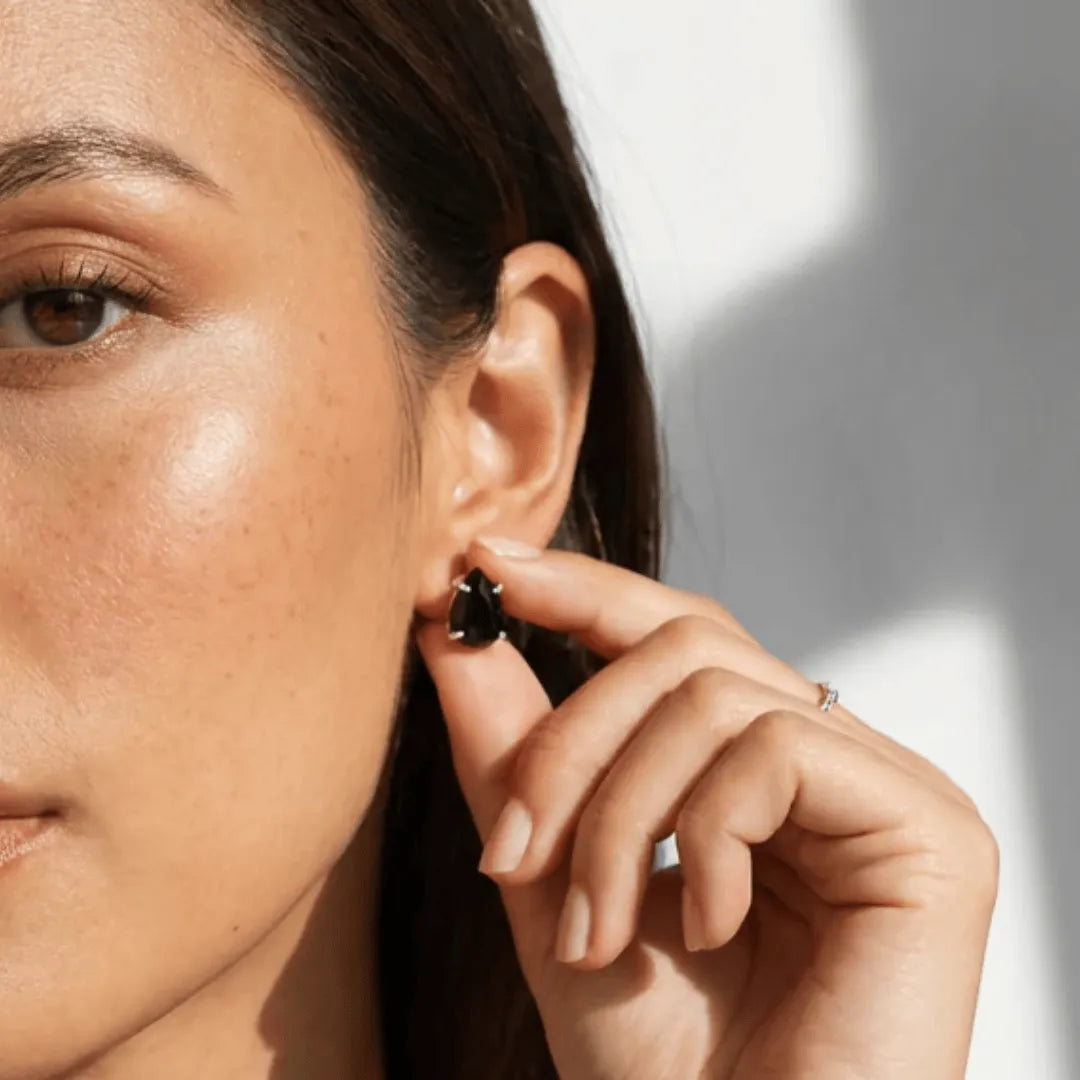 Close-up of a woman adjusting an earring with a neutral background