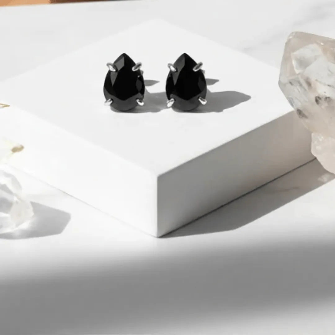 Black teardrop earrings on a white surface with a soft focus background