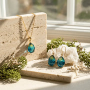 Blue teardrop earrings on a stone surface with greenery