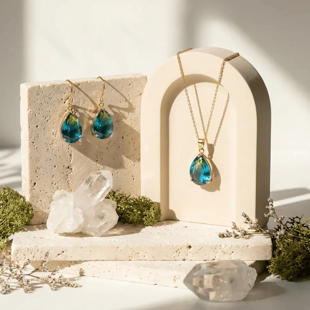 Jewelry set with blue teardrop-shaped pendants on a decorative stand with crystals and plants.