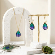 Jewelry set with necklace and earrings on a decorative stand with peacock feather and moss.