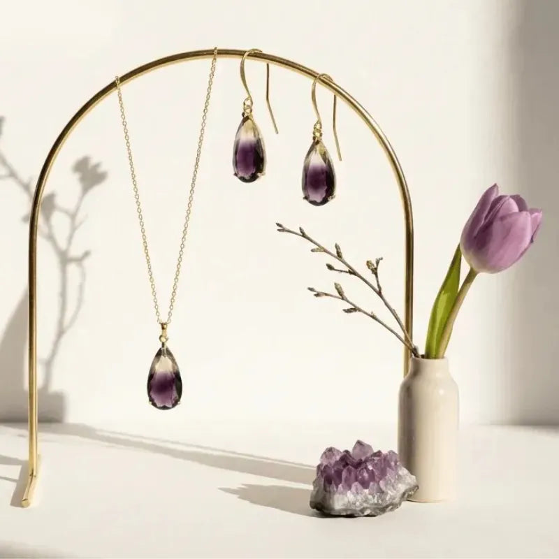 Amethyst jewelry set with necklace and earrings on a gold stand, next to a vase  