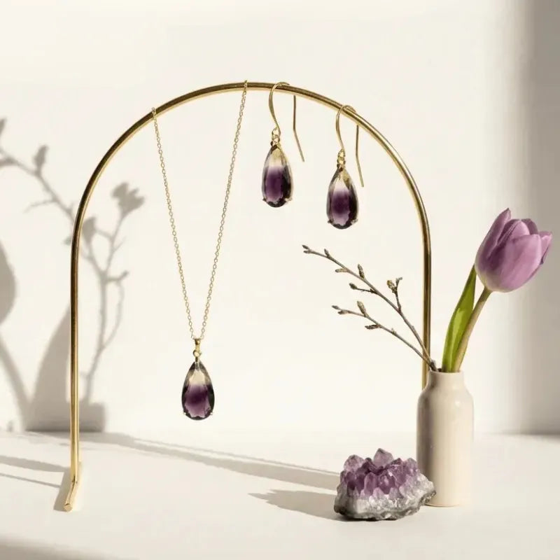 Jewelry set with necklace and earrings on a gold stand, next to a vase with a purple tulip and amethyst crystal.
