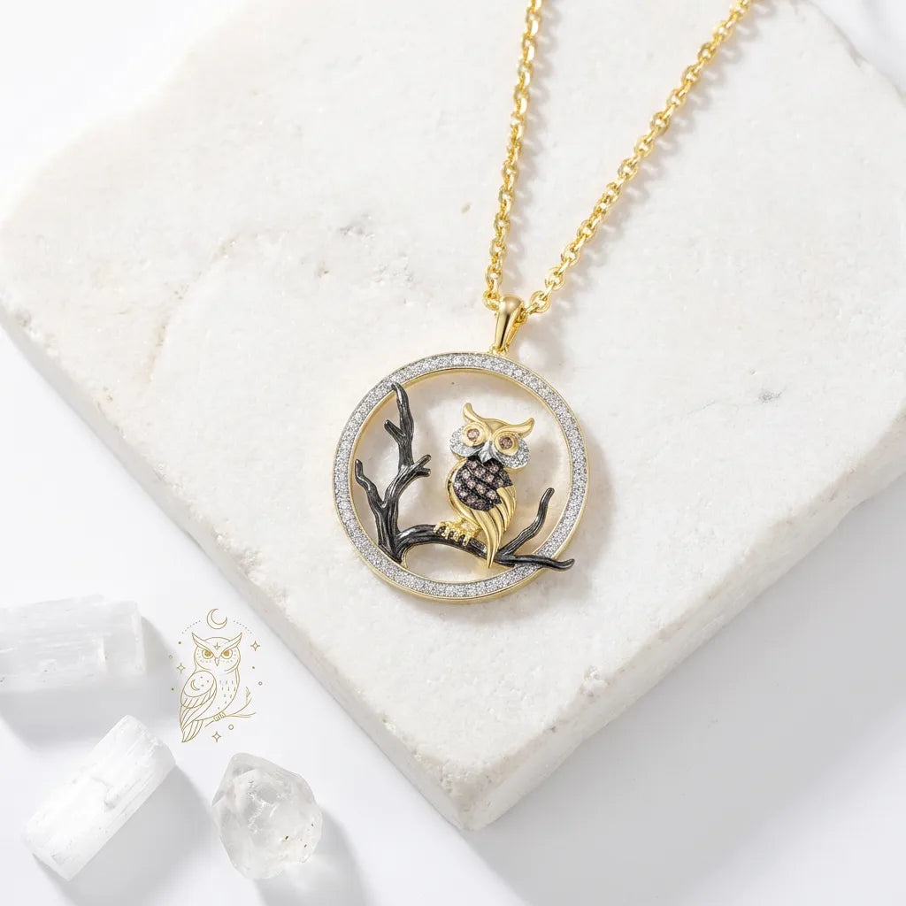 Gold owl pendant necklace on a white marble surface with 'owl' logo.
