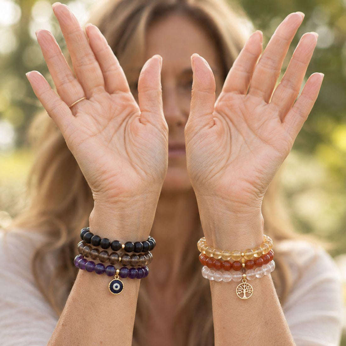 A close-up lifestyle shot of a woman's hands and wrists, showing multiple beaded bracelets. 