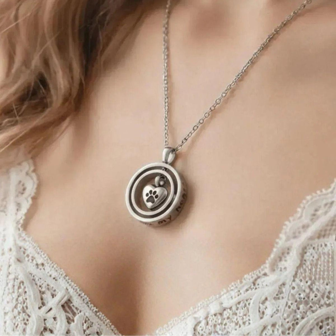 A close-up of a silver circular pendant necklace worn on a model's neck. The pendant features a small paw print
