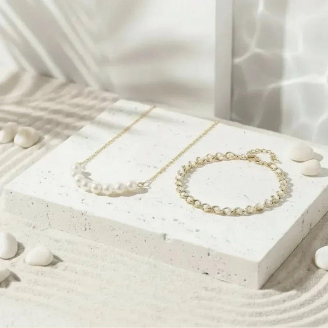 Gold pearl in bracelet and necklace on a white stone with water reflection