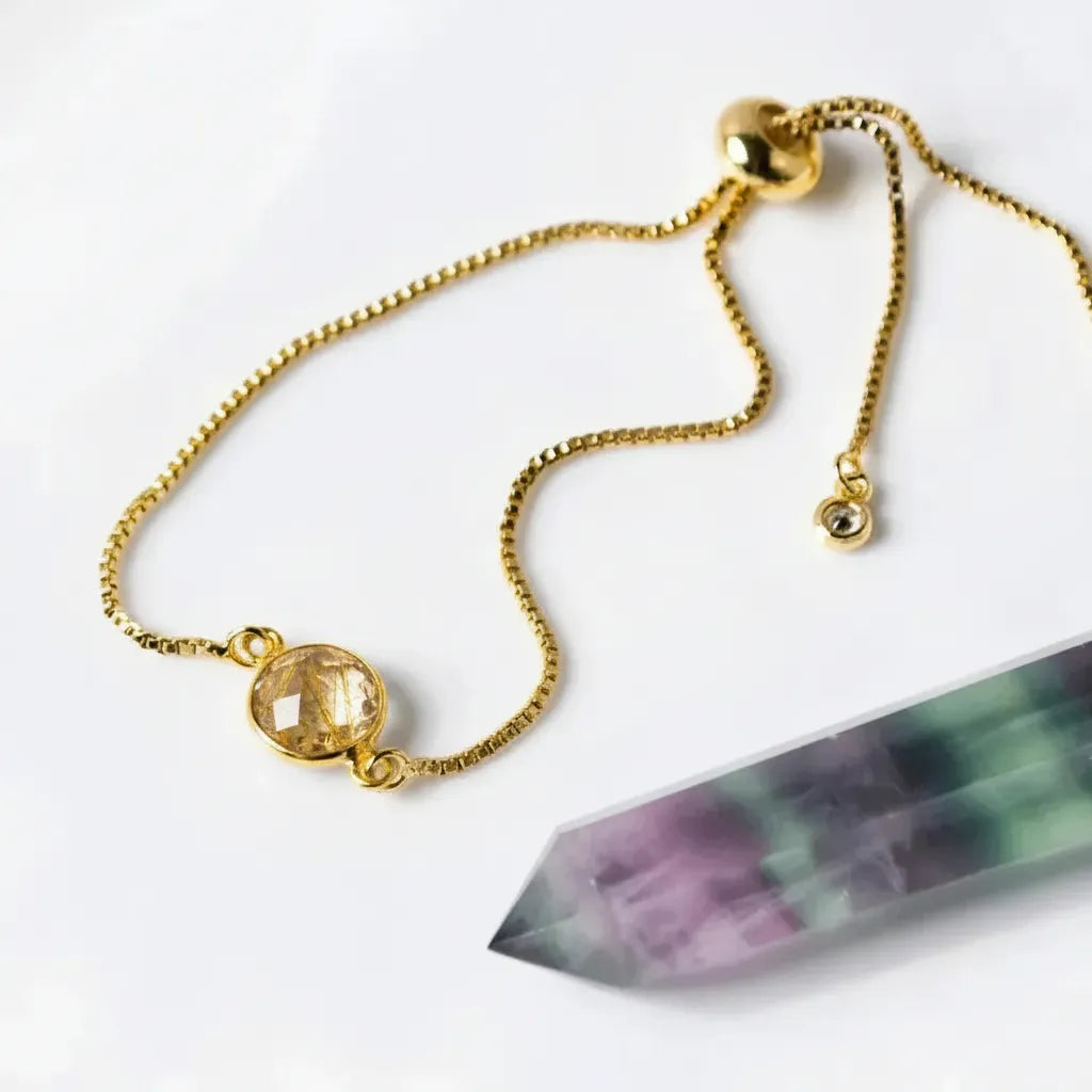 Gold bracelet with a yellow gemstone pendant on a white background