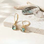 Gold earrings with green gemstones on a sandy surface