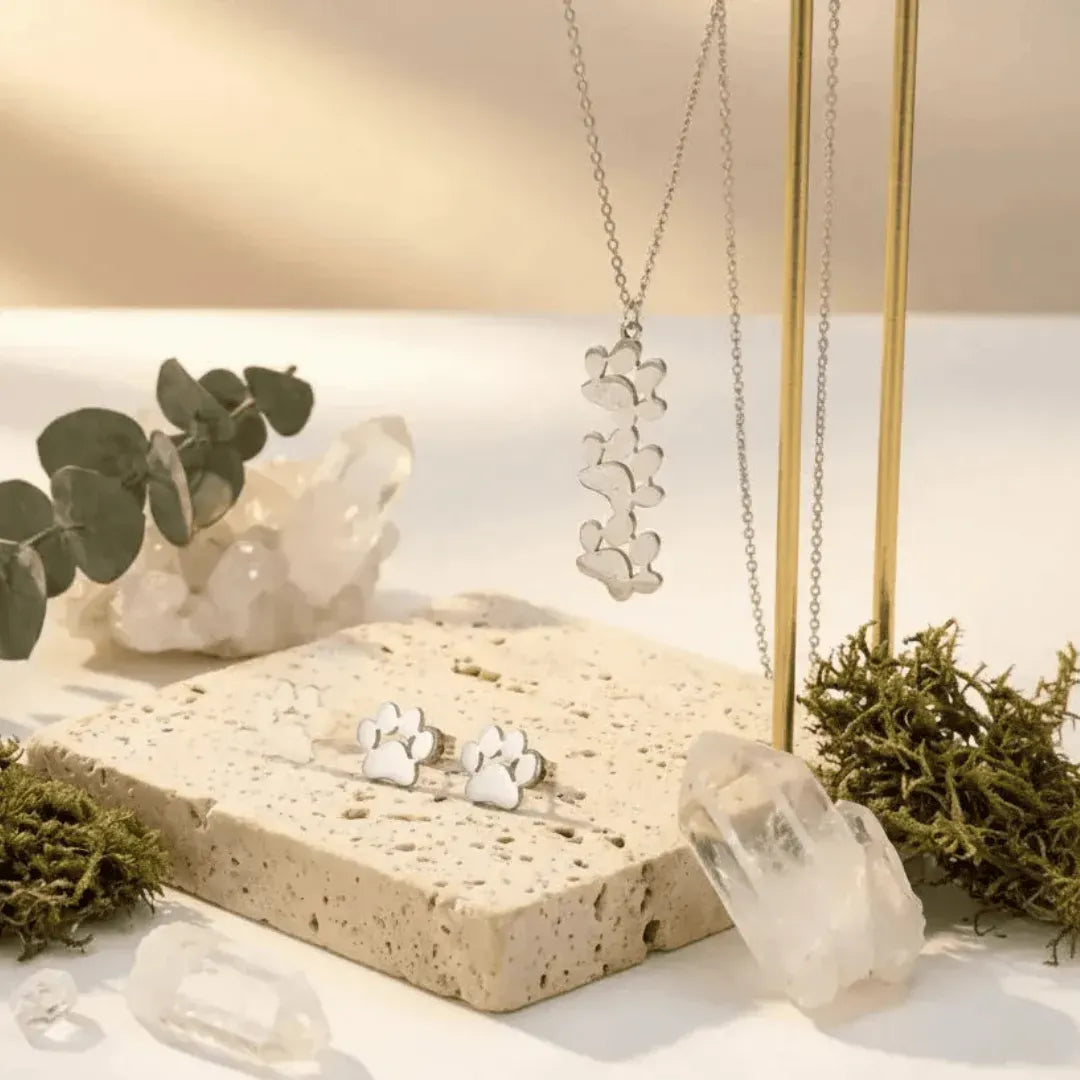 Silver jewelry set including necklace and earrings on a stone surface with plants.