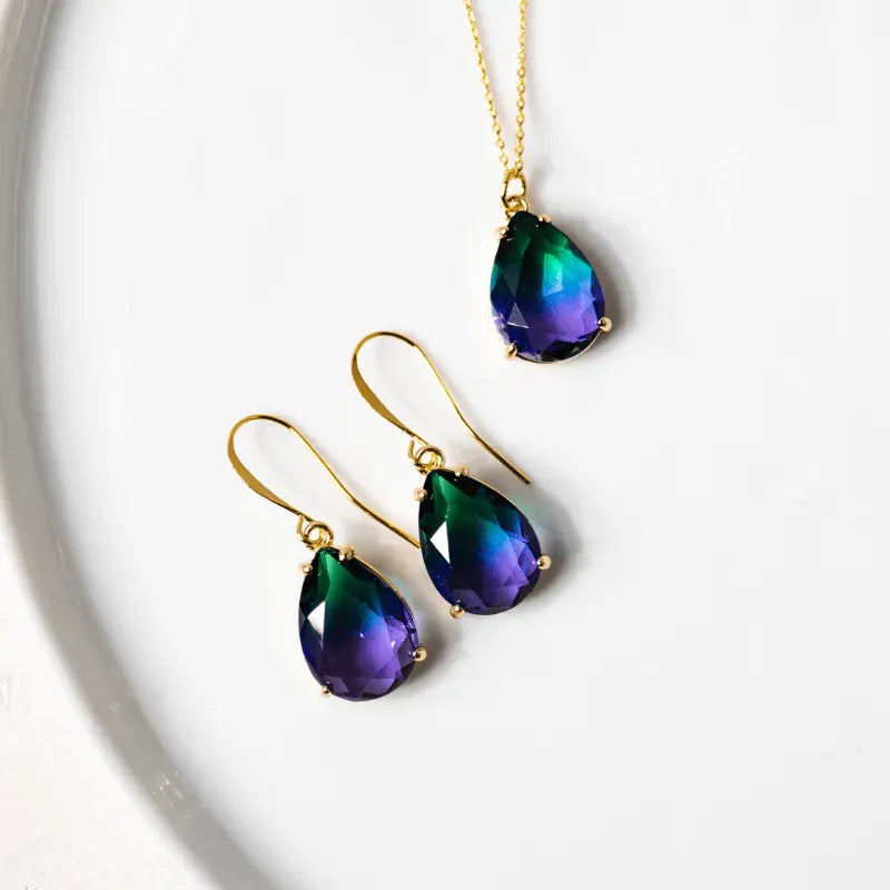 Teardrop-shaped jewelry set with purple and green stones on a white background
