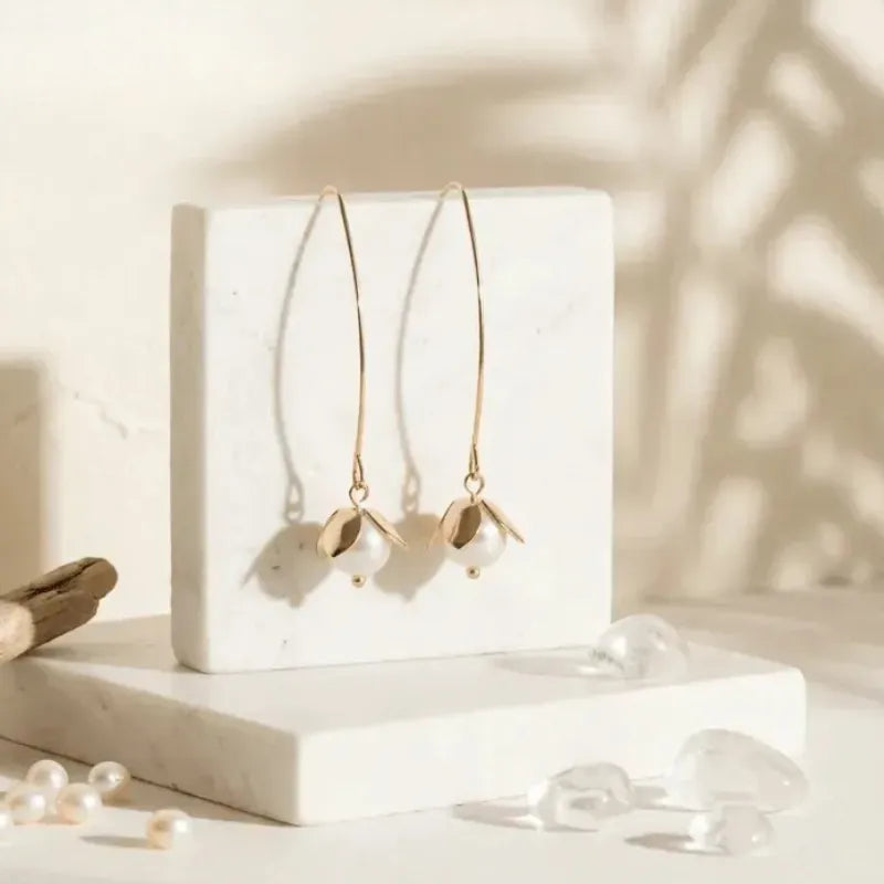 Gold earrings with pearls on a white block against a neutral background
