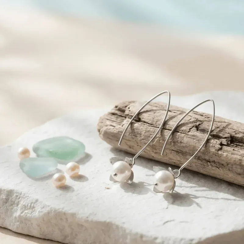 Pearl earrings on a stone with sea glass and driftwood