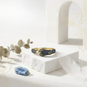 Gold ring with blue gemstones on a white surface with eucalyptus leaves