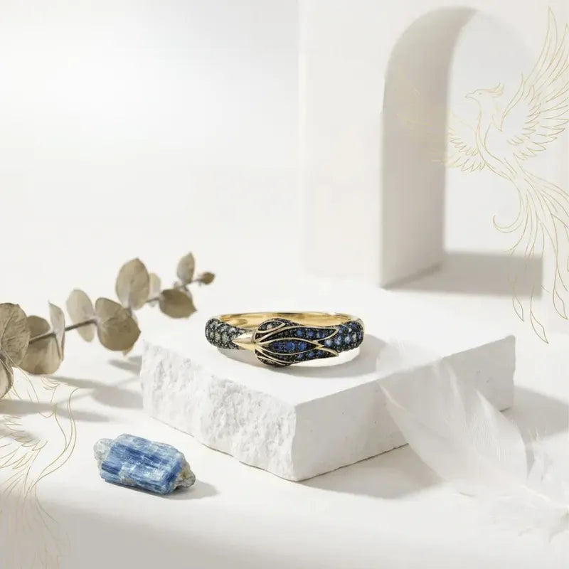 Gold ring with blue gemstones on a white surface with eucalyptus leaves