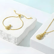 Gold pineapple bracelet and necklace on a white and light blue background