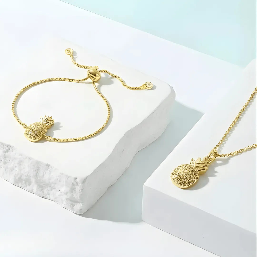 Gold pineapple bracelet and necklace on a white and light blue background