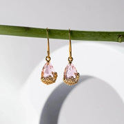 Gold earrings with pink teardrop-shaped gemstones hanging on a green branch against a light background