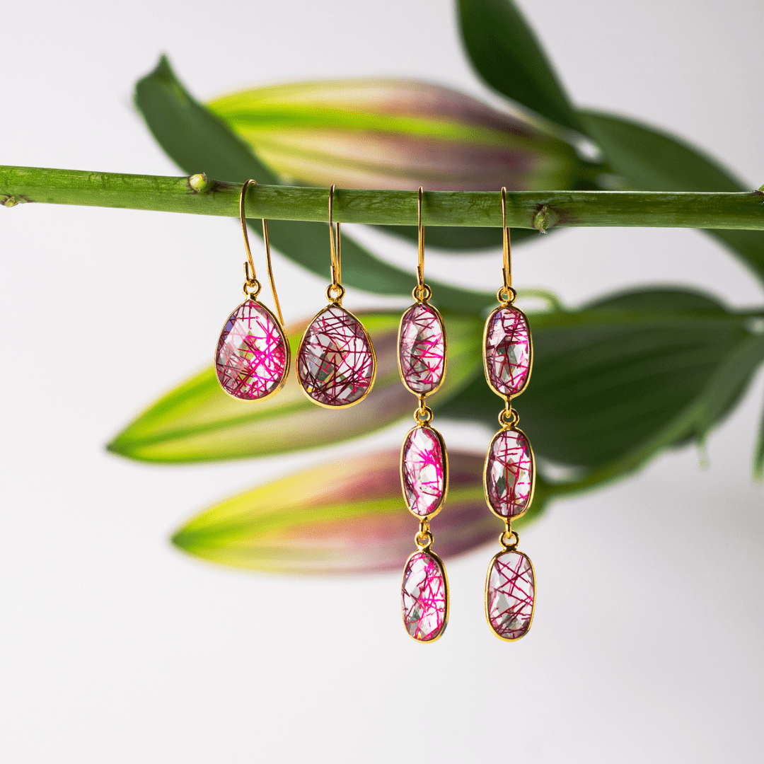 Pink teardrop earrings with gold hooks on a branch with leaves