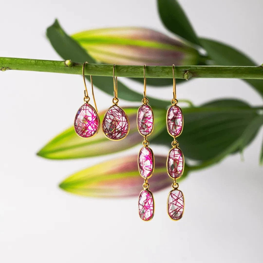 Pink teardrop earrings with gold hooks on a branch with leaves
