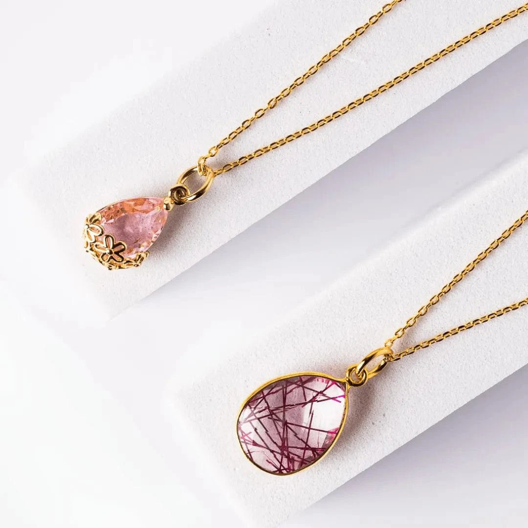 Two gold necklaces with pink stone pendants on a white background