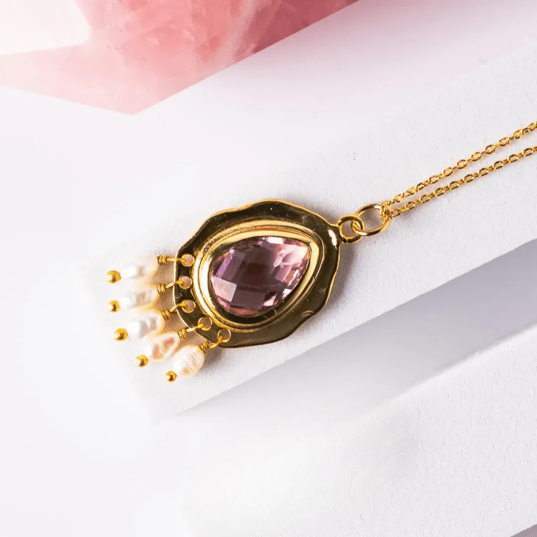 Gold necklace with a pink gemstone pendant on a white background