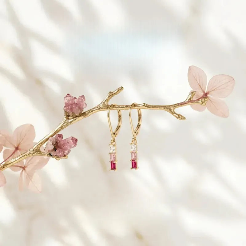 Gold branch with pink flowers and red earrings on a soft background