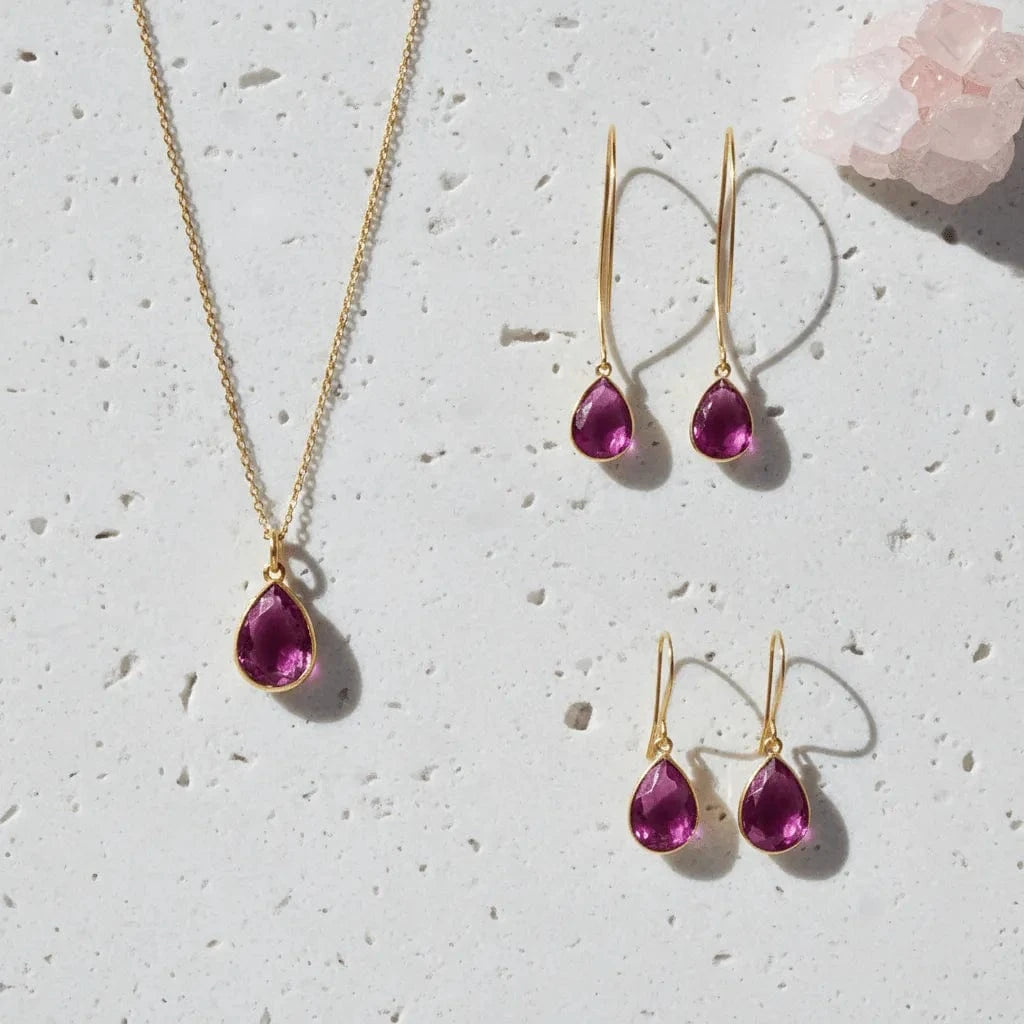 Gold jewelry set with pink gemstones on a light gray surface