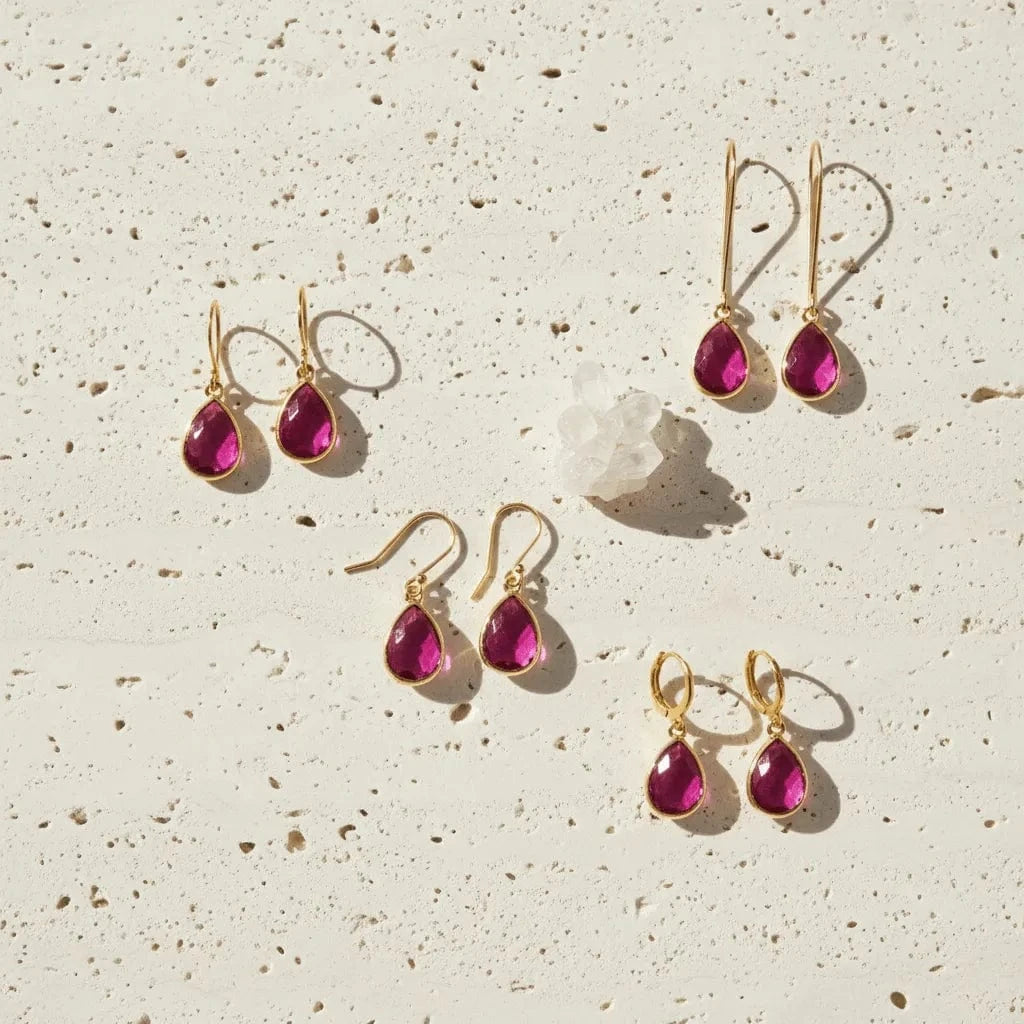Gold earrings with pink gemstones on a textured beige surface