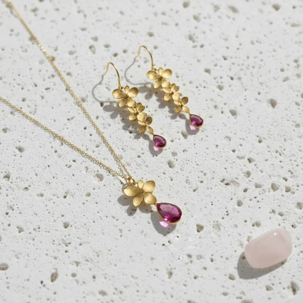 Gold necklace and earrings with pink gemstones on a textured surface