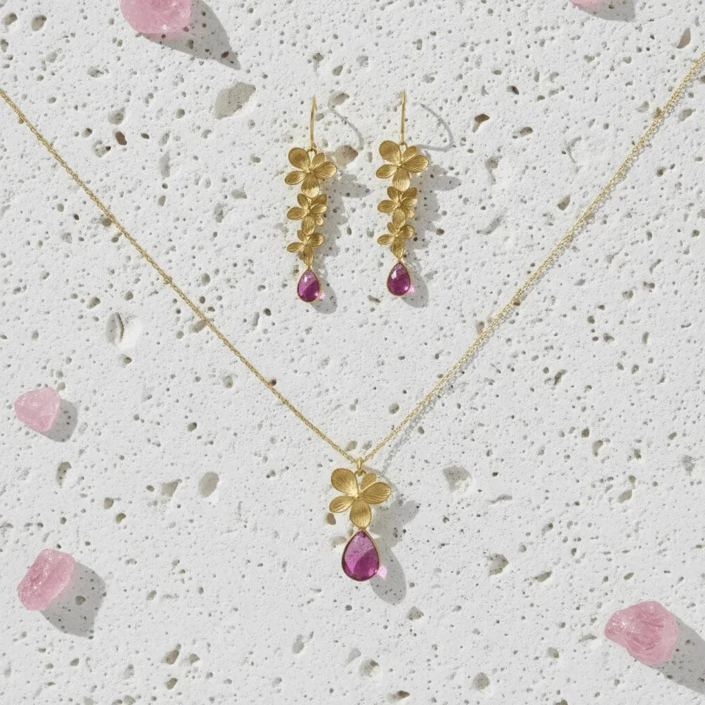 Gold necklace with pink gemstones on a textured white surface
