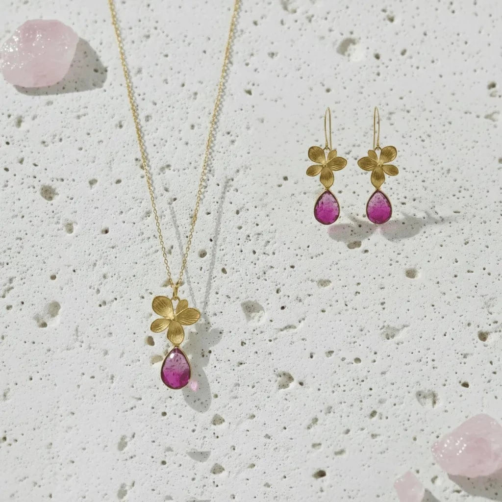 Gold necklace and earrings with pink teardrop stones on a textured white background