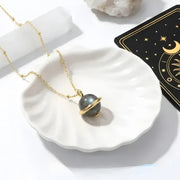 Gold necklace with a black sphere pendant on a white dish, with a tarot card in the background.