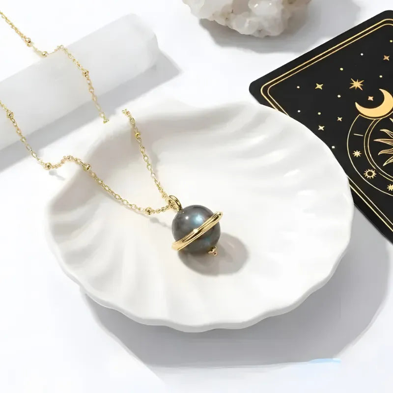 Gold necklace with a black sphere pendant on a white dish, with a tarot card in the background.