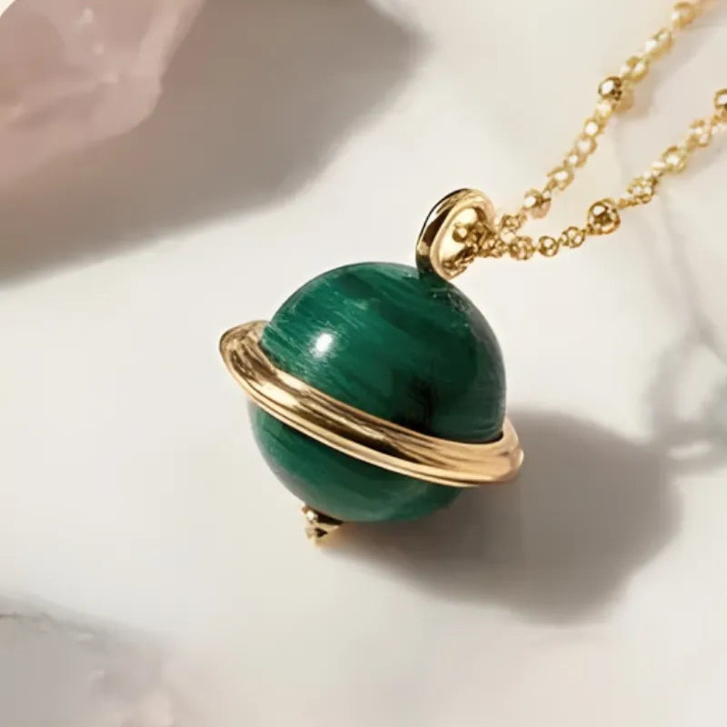 Green planet-shaped pendant on a gold chain against a light background