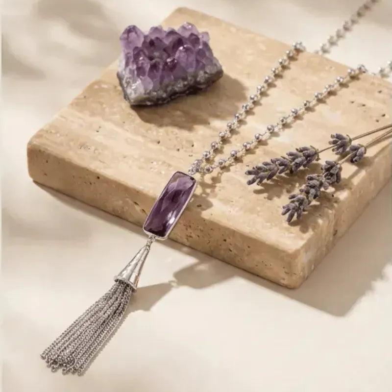 Necklace with a purple pendant on a stone surface with lavender and an amethyst crystal.