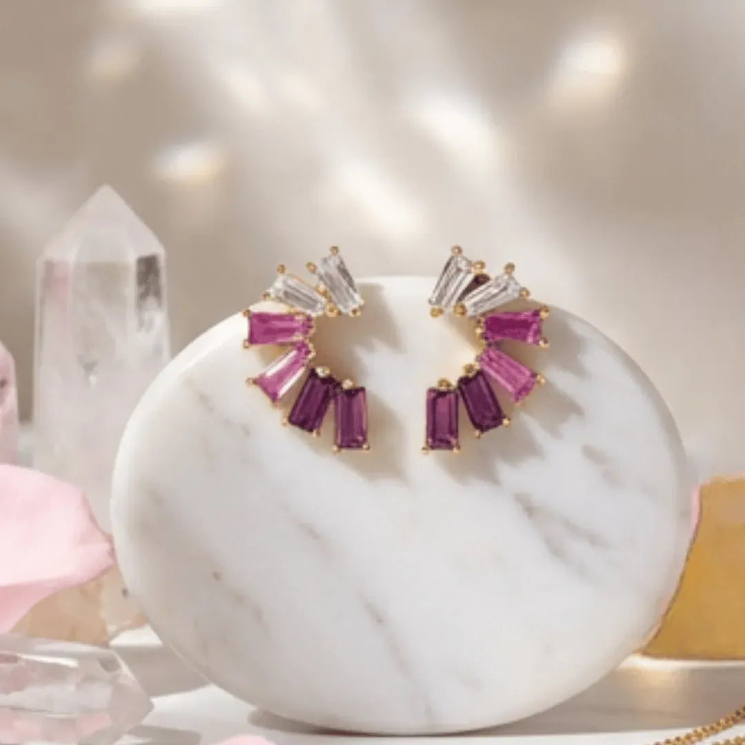 Earrings with pink and purple gemstones on a marble surface with crystals in the background