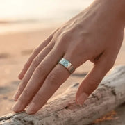 Hand wearing a ring with a sunset or sunrise in the background