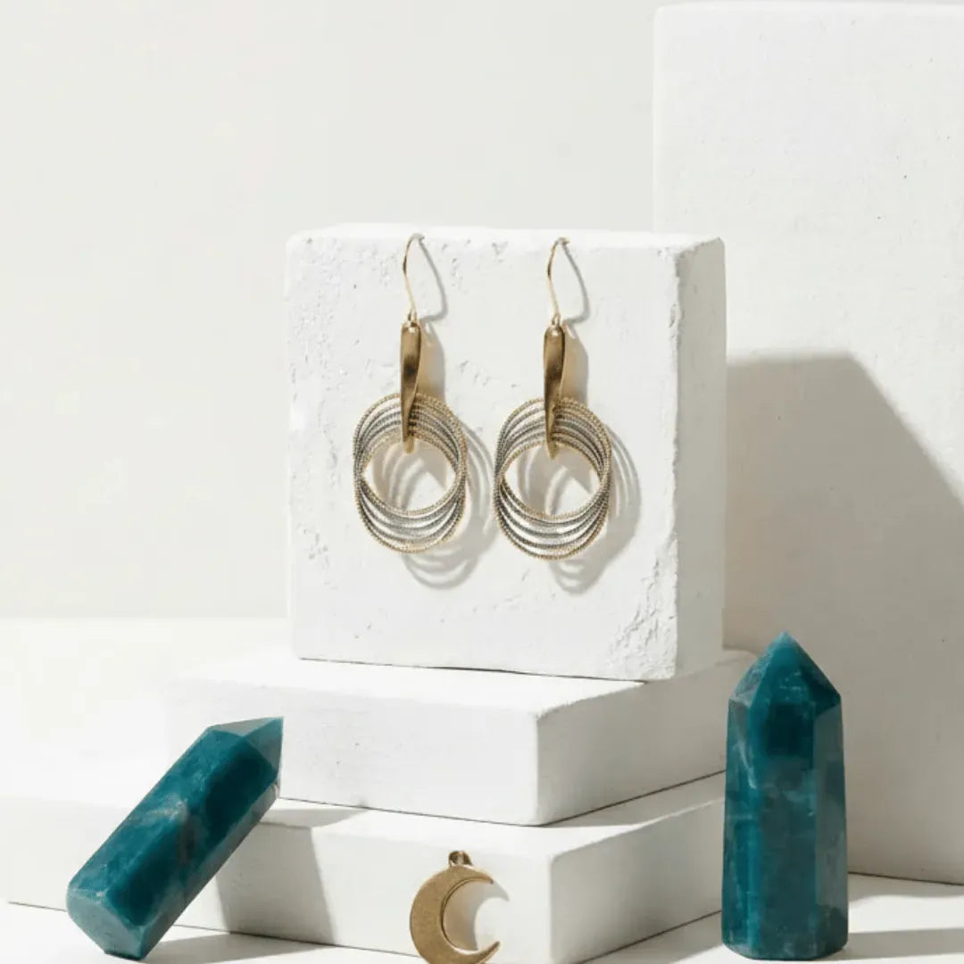 Gold hoop earrings on a white stand with teal crystals on a light background