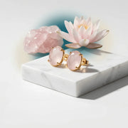 Rose quartz earrings with gold accents on a marble surface with decorative flowers.