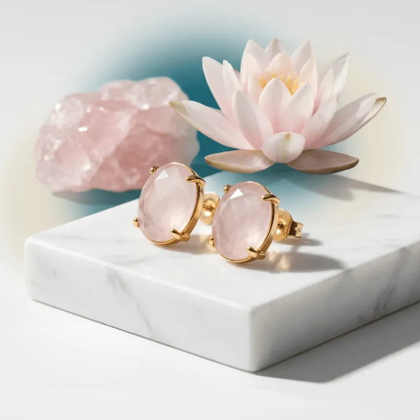 Rose quartz earrings with gold accents on a marble surface with decorative flowers.