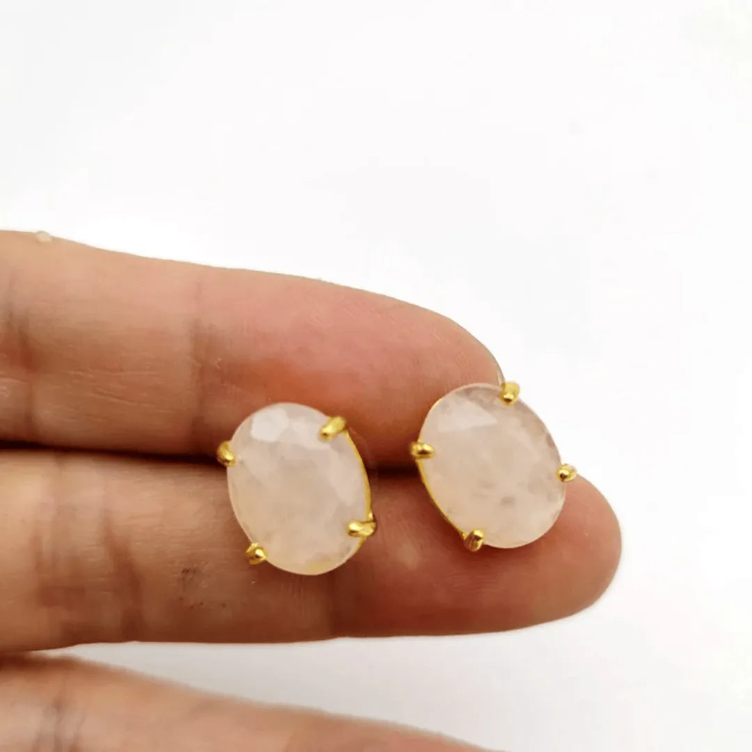 Gold earrings with pink stones held between fingers on a white background