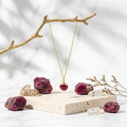 Gold necklace with pendant on a stone stand with red crystals and branches.