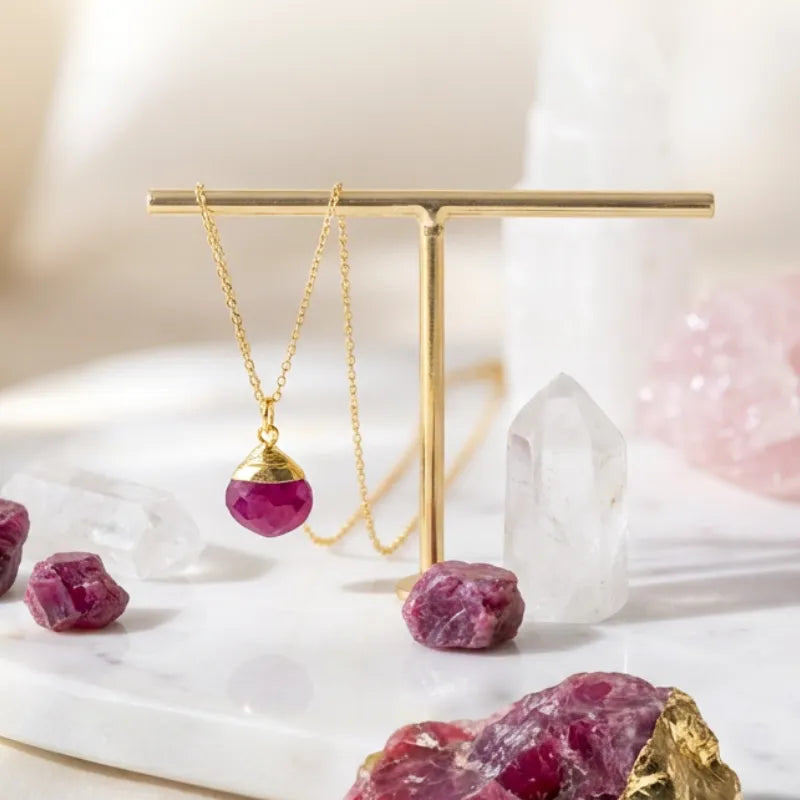 Gold necklace with a red pendant on a marble surface with crystals